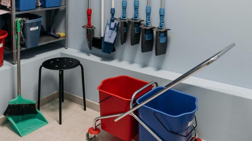 Neatly arranged cleaning tools in a storage room with mops, buckets, and shelving.